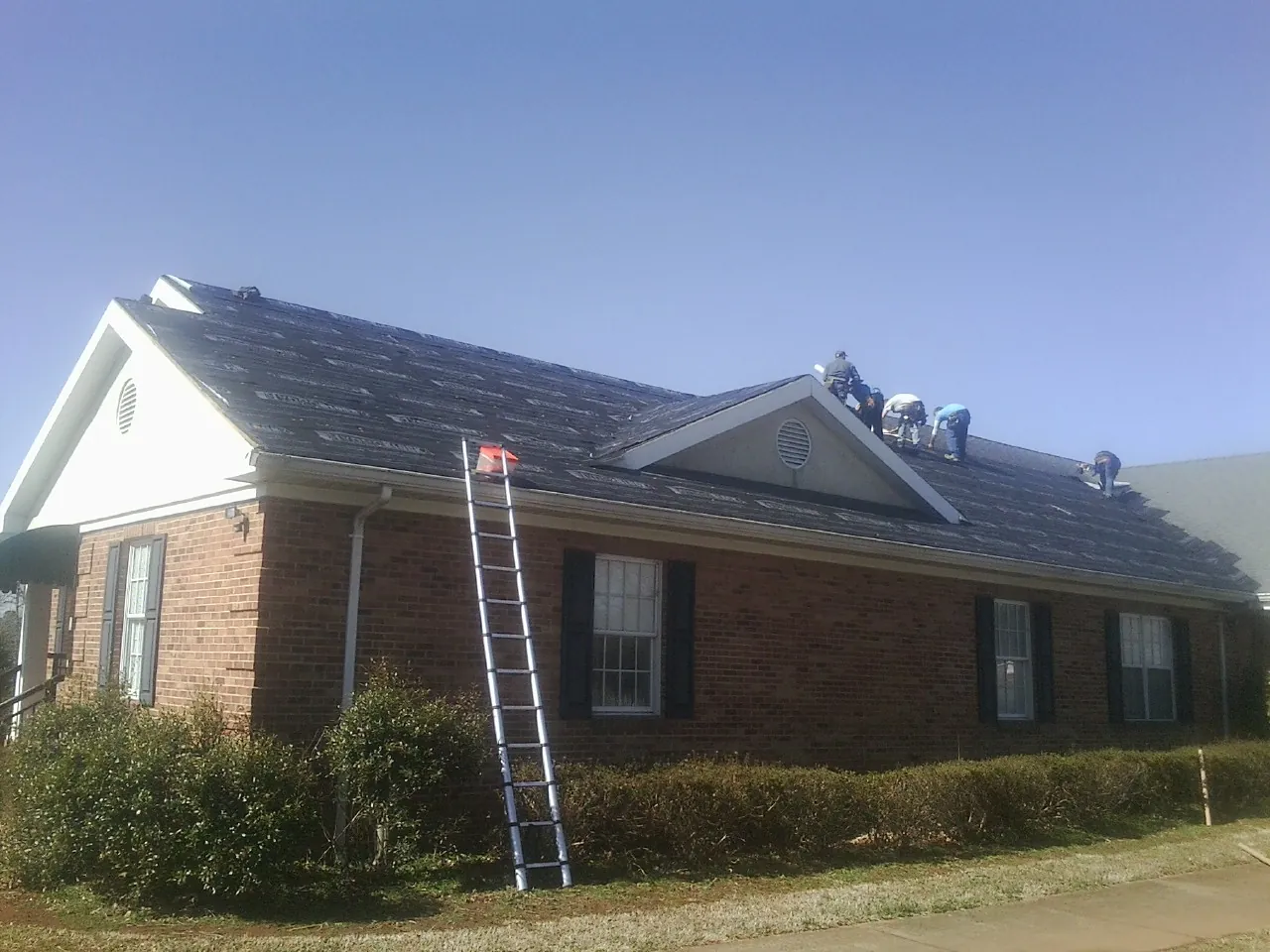 Crew tearing shingles off a brick ranch roof with a ladder set — Emergency Roof Repair work by our crew in Bayview