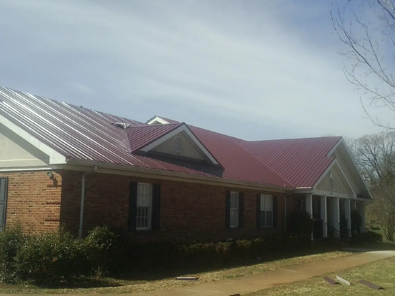 Red metal roof with gabled entries on a long brick building, from a Hail Damage Roof Repair job in Bayview