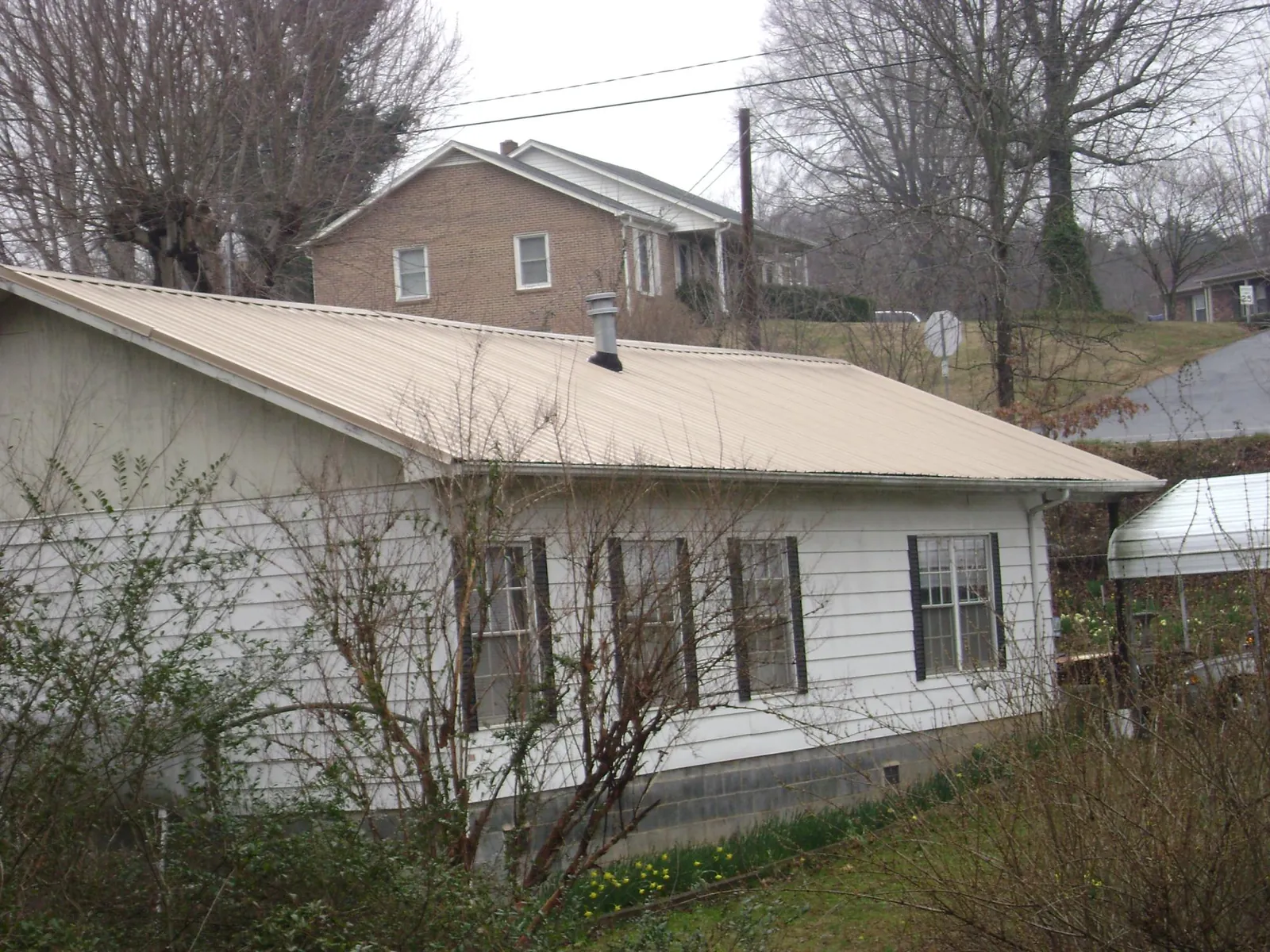 Tan metal roof on a white sided house set into a hillside — Commercial Roofing by Roofing Brothers in Bayview